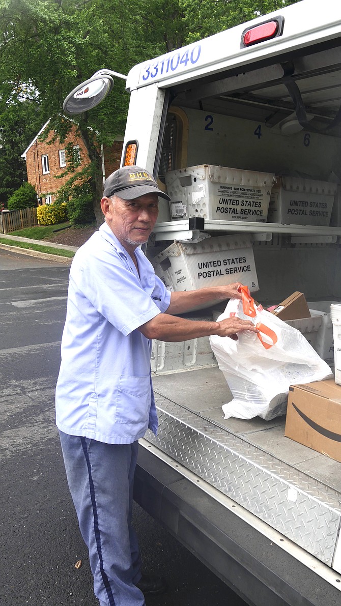 A letter carrier picks up his first sack of donated canned tuna and cereal at a front door at the beginning of his mail delivery route Saturday, May 13th. He puts the bag in the empty space in the back of his truck between his packages and letters ready for delivery. He says he expects the truck to be full of donations for AFAC at the end of the route. “But after I deliver them to the post office, I have another route today so will be going back out again.”