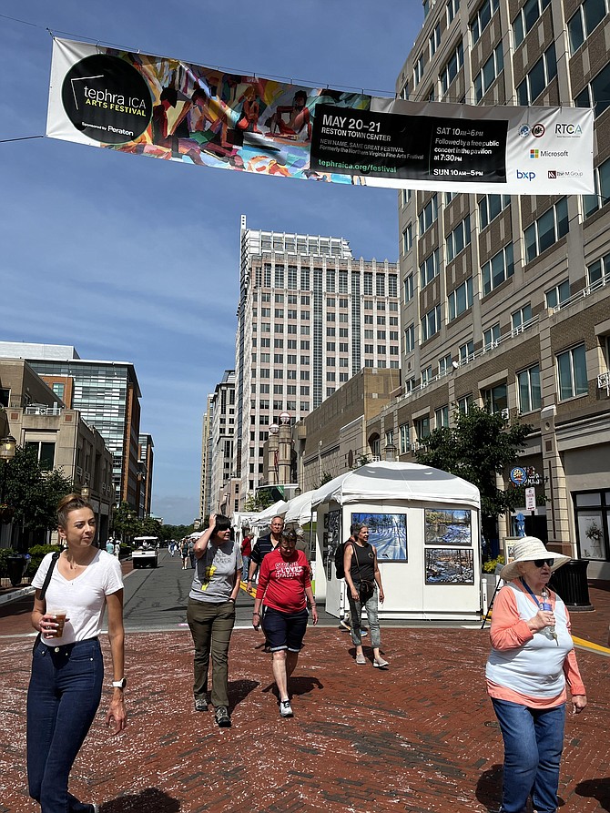 Visitors to the Tephra ICA Arts Festival 2023 pass beneath the street banner in Reston Town Center that announces the festival's activities and the event's sponsor, Peraton.