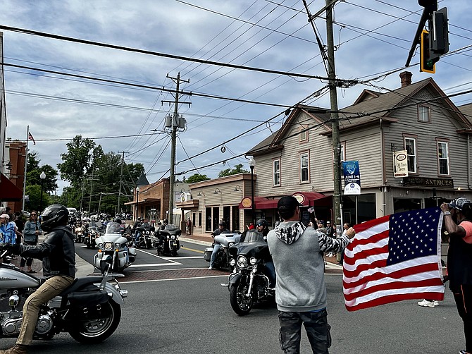 Sixty-some motorcycles with about 80 riders pass by the U.S. flag held across Elden Street in Herndon and roll through town two-by-two, cruising toward Great Falls and the George Washington Parkway. They will conclude their ride at the Vietnam Veterans Memorial to honor and remember those who died in the war.