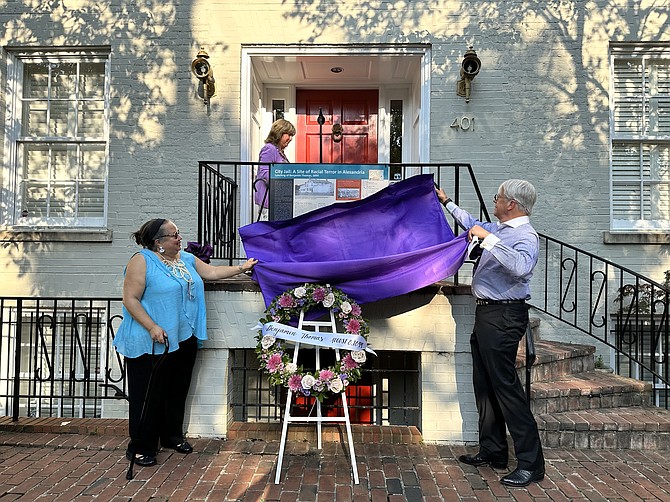 Audrey Davis of the Alexandria Community Remembrance Project, left, joins homeowner Walter Steimel in unveiling a temporary plaque Aug. 8 at 401 N. St. Asaph Street. A permanent plaque will commemorate the site of the former city jail where a mob dragged 16-year-old Benjamin Thomas out of his cell to be lynched a few blocks away.
