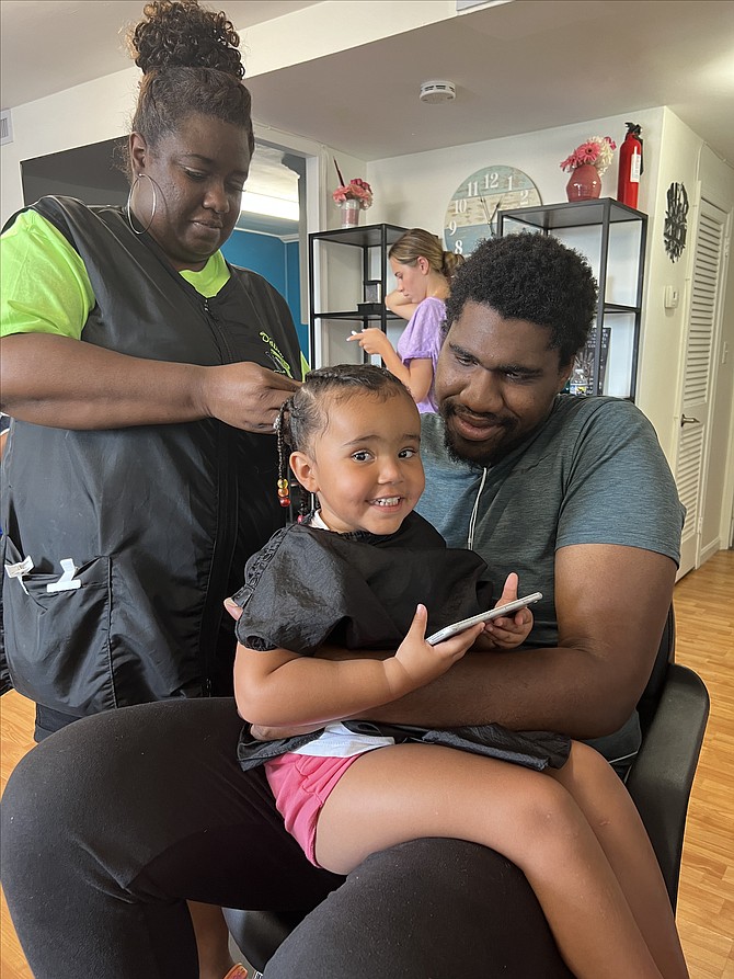 Vonzel Martenia holds his daughter Zelena, 3, as stylist Dellice Harris gives her a new look to start off the school year during a free styling day for Carpenter’s Shelter girls Aug. 14 at Iye’s Salon at 4600 Duke Street.