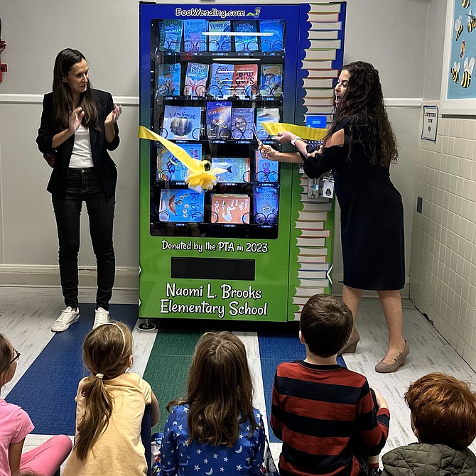 Principal Suzanne Hess, right, cuts the ribbon on the new book vending machine Oct. 12 at Naomi L. Brooks Elementary School as past PTA president Arvita Cohen and students look on.