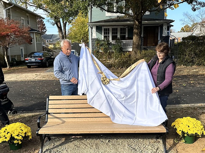Retired sheriff Dana Lawhorne, left, and Lori Knoernschild unveil a bench dedicated to Lawhorne and his childhood friend Tommy Knoernschild Nov. 12 in Del Ray. Tommy Knoernschild, whose childhood home is in the background, died in 2018 at the age of 58.