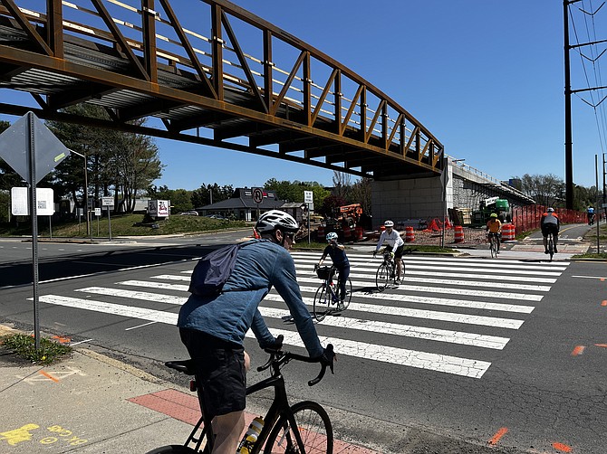Cyclists use the Wiehle Avenue (Rte. 828) at the W&OD trail crosswalk while above them looms the new but not operational pedestrian and bicyclist bridge.