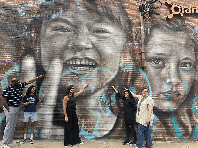 Alexandria City High School campus administrator Ashley Carter Sinclair, far left, with mural artist Nicole Bourgea, center, and attendees celebrating the unveiling of the Peace and Childhood Innocence mural May 30 at Bradlee Shopping Center.