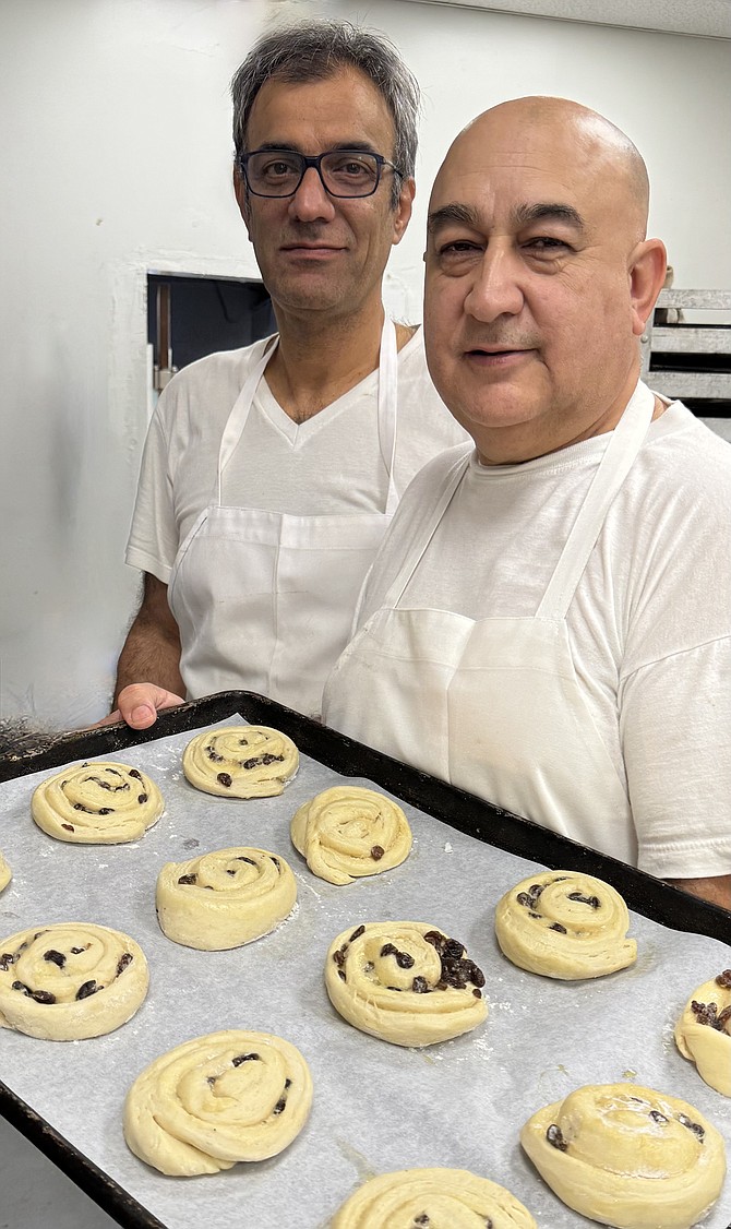 Owner/baker Max Malek (right), with new baking assistant Edalatian Zakeri, prepare a tray of raisin cinnamon buns for the oven