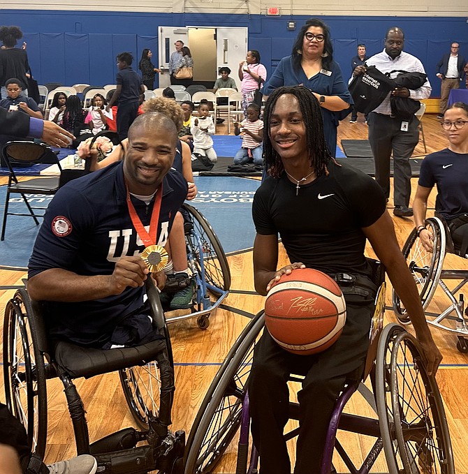 Trevon Jenifer, left, displays his gold medal from the Paris Olympics after signing a basketball for a fellow wheelchair athlete Sept. 18 at the Dunbar Alexandria-Olympic Boys and Girls Club.