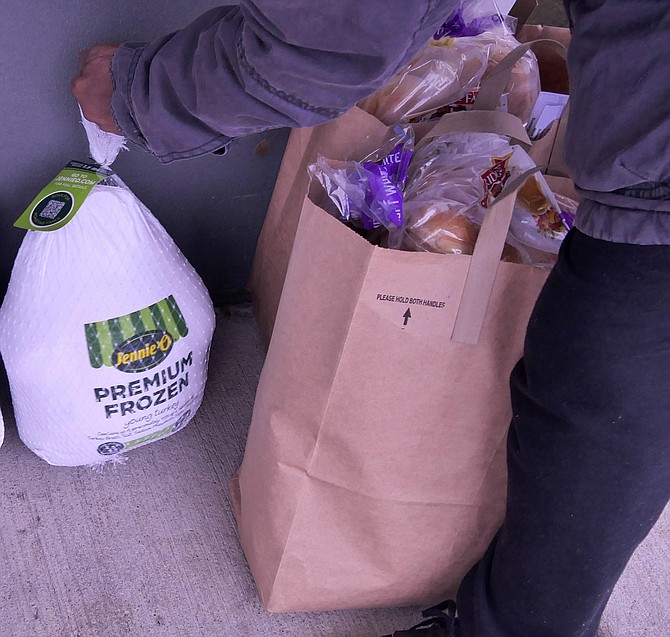 The last person in line at Thursday’s Turkey Week gathers up her bag of supplemental groceries and her heavy Thanksgiving turkey.