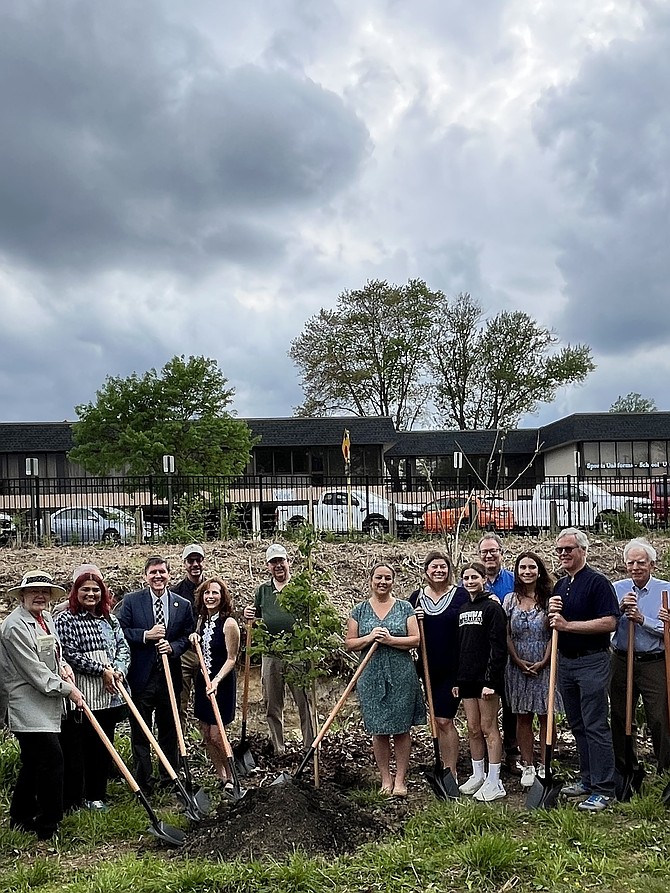 Linda Colbert, mayor of the Town of Vienna (black dress, white trim), stands beside Supervisor Walter Alcorn, while to her left is Del. Holly Seibold. They and others prepare to plant the seven redbud trees. Behind them is 125 Church Street, an obsolete office building adjacent to the  W&OD Park (Trail) with no existing tenants. A study is underway on the feasibility of razing it and building a W&OD Trail Visitor Center.
