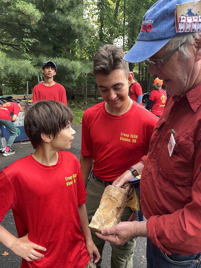 Chuck Anderson, Vienna250 co-chair and Vienna town councilmember, shows two Scouts of Troop 1539 in Vienna the pressed footprint of an infant centered in the clay before the 18th-century brick was sun-dried in wooden forms and then fired in a kiln.