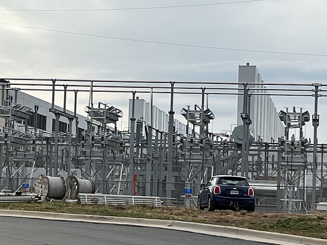 Representative Example: A high-voltage substation and backup generator array serving an existing data center in the Sully Square area of Herndon illustrates the scale of power infrastructure supporting data facilities in Fairfax County. The metal framing, insulators, overhead tubular buses, and switching equipment represent classic open-air substation design, positioned in front of a windowless data center building. (Note: Photo shows a Herndon facility and is not the proposed Edsall Road project in Mason District.)
